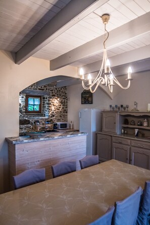 A kitchen with a stone wall, wooden ceiling beams, a chandelier, and a dining area with a table and chairs.