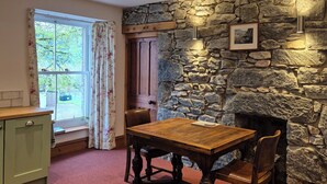 A room with a stone wall, a fireplace, a wooden table with chairs, a window with curtains, and a green cabinet. - No.3 The Old Convent. (Fort Augustus)
