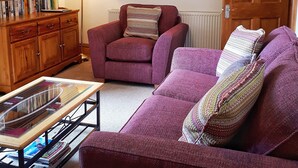 A living room with a wooden bookshelf, a red armchair, a purple sofa, and a glass coffee table. - No.3 The Old Convent. (Fort Augustus)