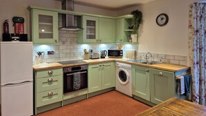 A compact kitchen with green cabinets, a microwave, a toaster, a sink, and a washing machine. - No.3 The Old Convent. (Fort Augustus)