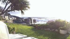 Un patio con sillas blancas que da a un litoral rocoso y olas del océano.