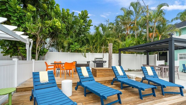 Een houten terras met blauwe lounge fauteuils, oranje stoelen en een barbecueplek.