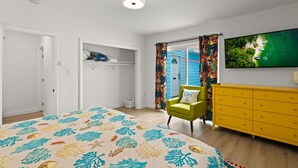 Een slaapkamer met een bed, een groene fauteuil, een gele dressoir en een televisie waarop een tropische scène wordt getoond.
