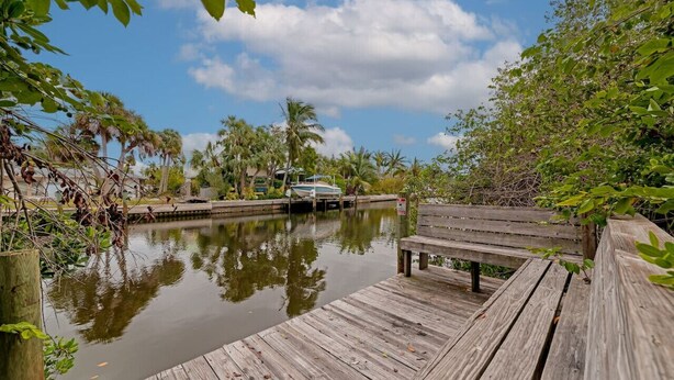 A wooden dock extending over calm water, surrounded by lush greenery and palm trees. - Walk to the Beach | Osprey Villa | Siesta Key (Sarasota)