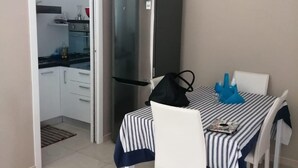 A compact kitchen with a refrigerator, a dining table with chairs, and a door leading to another room.