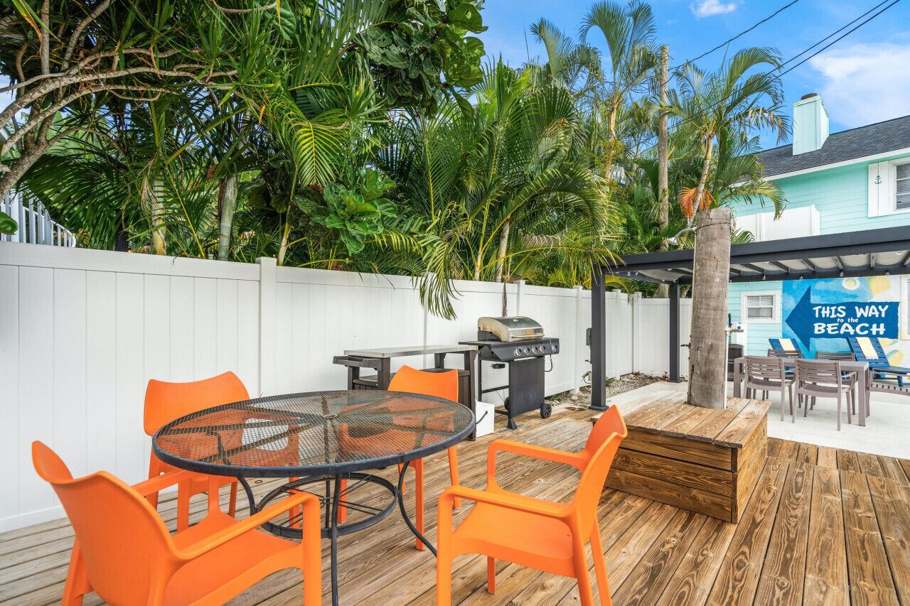 Une terrasse avec une table ronde et des chaises orange, un barbecue et une plateforme en bois.