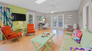 A living room with a green sofa, orange chairs, a small table, and a ceiling fan. - Key West Villa 3 min to #1 Beach • Pool • BBQ (Sarasota)