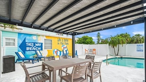 An outdoor pool area with lounge chairs and a table, a mural with beach and flip flops theme, and a pool with a 'No Diving' sign. - Key West Villa 3 min to #1 Beach • Pool • BBQ (Sarasota)