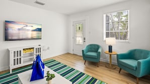 A modern living room with a flat-screen TV, teal armchairs, a striped rug, and a white cabinet with yellow items. - Dolphin Villa - Pool - Steps to Siesta Key Village (Sarasota)