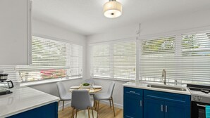 A modern kitchen with a dining area, featuring a white countertop, blue cabinets, and a round table with chairs. - Dolphin Villa - Pool - Steps to Siesta Key Village (Sarasota)