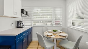 A modern kitchen with white cabinets, a blue countertop, and a dining area with a round table and grey chairs. - Dolphin Villa - Pool - Steps to Siesta Key Village (Sarasota)