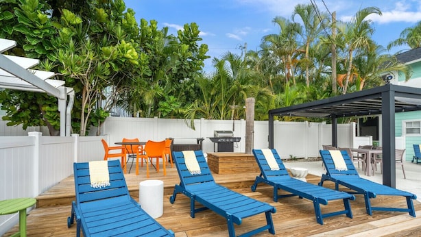 A wooden deck with blue lounge chairs, orange chairs, and a barbecue area. - Dolphin Villa - Pool - Steps to Siesta Key Village (Sarasota)