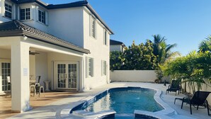 Ein Poolbereich mit Whirlpool, Sitzgelegenheiten im Freien und einem Gebäude mit großen Fenstern und einer überdachten Terrasse.