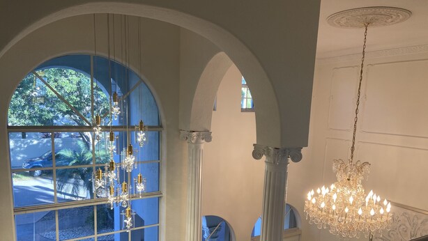 Eine prächtige Treppe mit einem Kronleuchter, Bogenfenstern mit dekorierter Glasverkleidung und Blick ins Freie.
