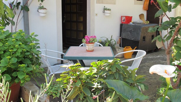 A patio with a table and chairs, surrounded by potted plants and a small garden. - Lovely Apartment With a Sea View Apartment (Supetar)