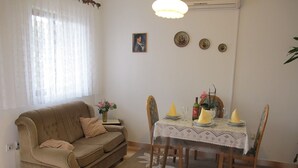 A living room with a sofa, dining table, chairs, and a small side table with a vase of flowers. - Lovely Apartment With a Sea View Apartment (Supetar)