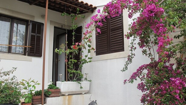 A building with a white facade, a wooden balcony, and a window with brown shutters. - Lovely Apartment With a Sea View Apartment (Supetar)