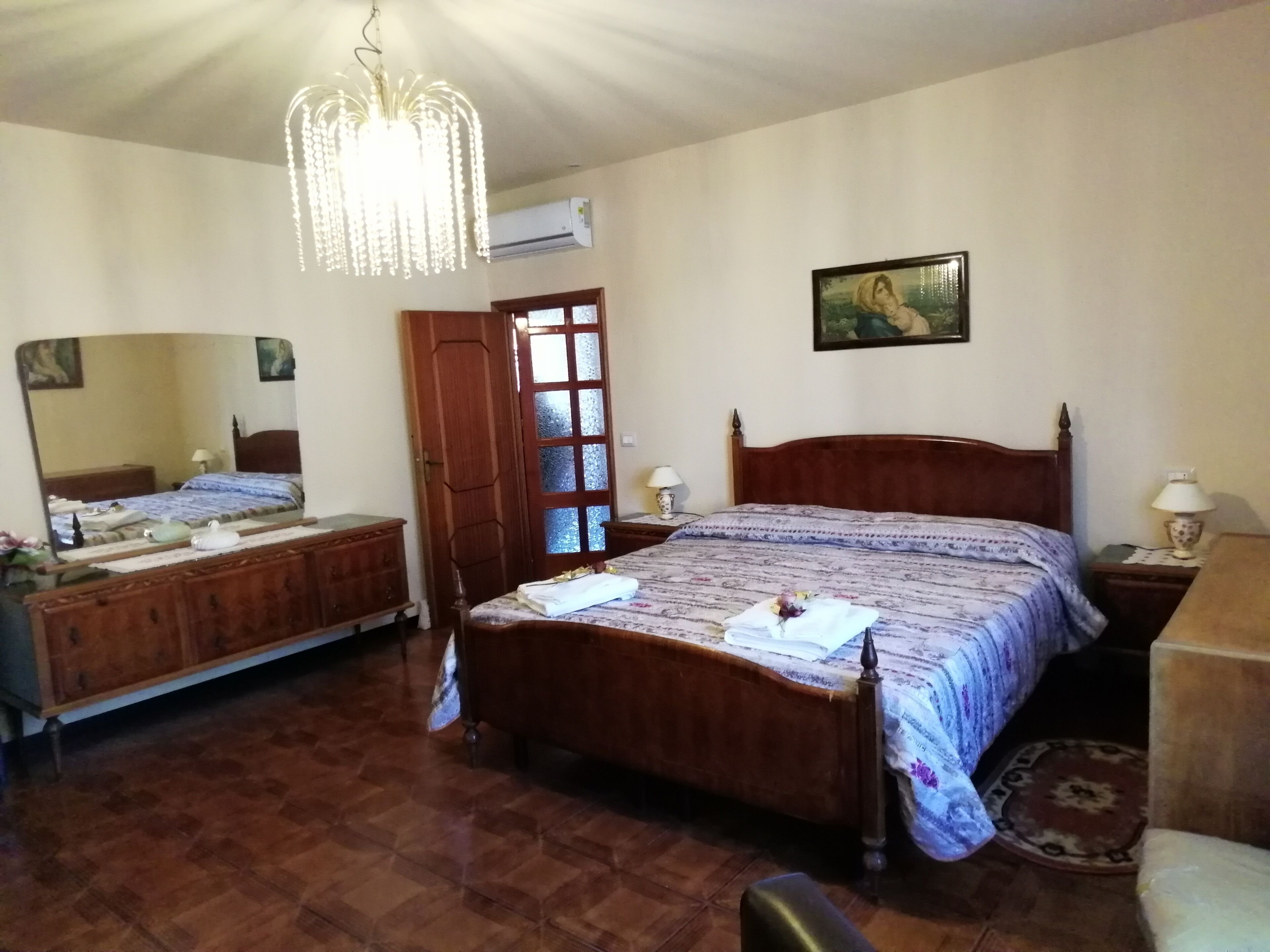 Ein Schlafzimmer mit einem hölzernen Bett, einem großen Spiegel, einer Kandelaberleuchte und einer Klimaanlage an der Wand.