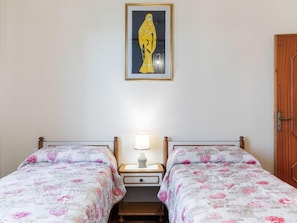 A bedroom with two beds, a nightstand with a lamp, and a framed artwork on the wall.