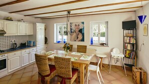 A kitchen with white cabinets, a dining table with chairs, a radiator, and a window with a view of the outdoors.