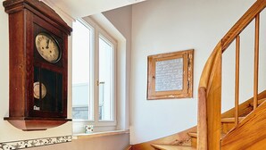 A wooden staircase with a handrail, a wall-mounted clock, and a window with a view.