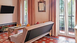 Una habitación con sofá, una mesa con objetos decorativos, un espejo y una ventana con cortinas.