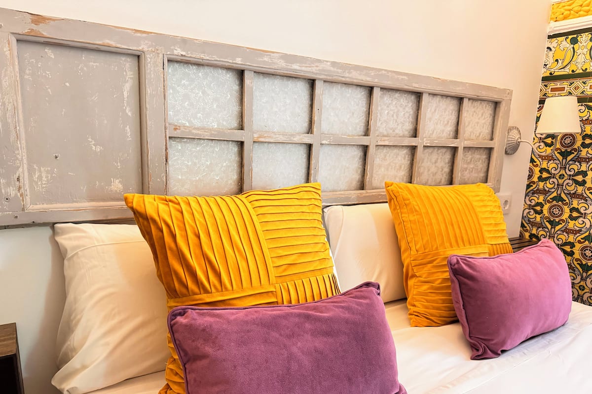 A bed with white and yellow pillows, a purple pillow, and a wooden headboard with a frosted glass panel.