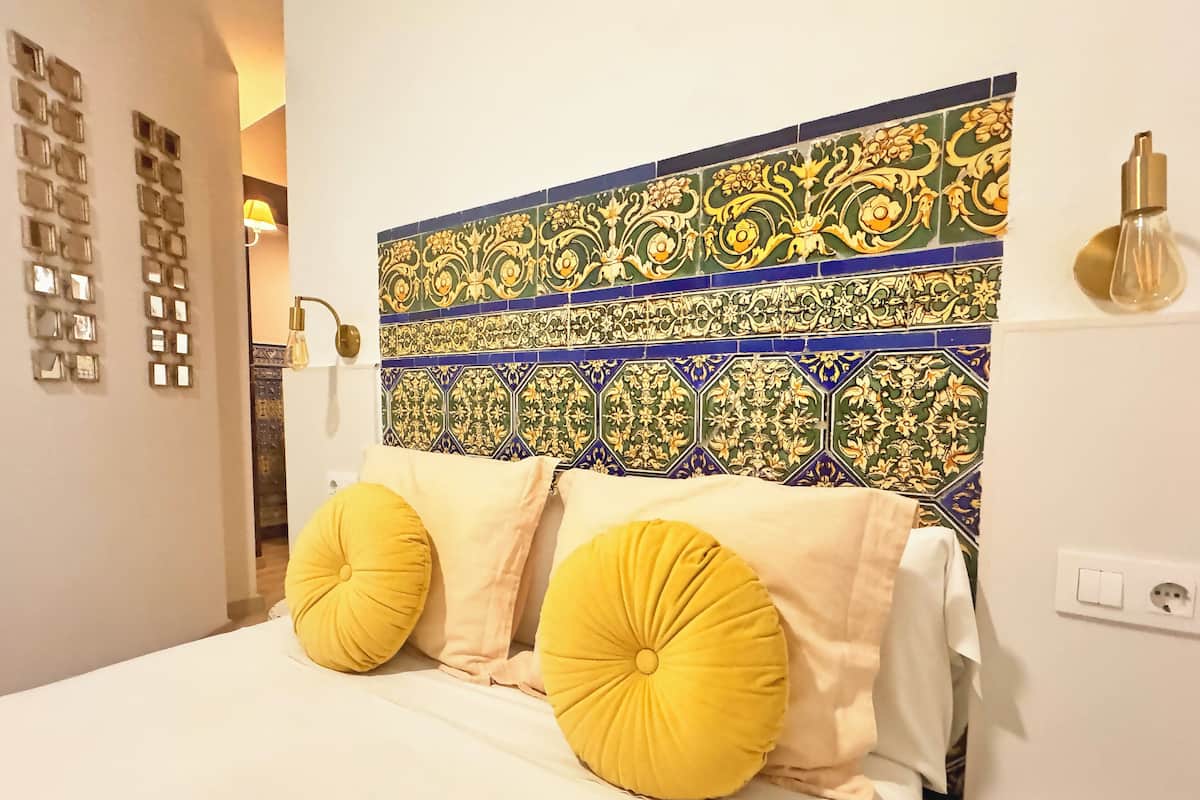 A bed with yellow pillows, a decorative headboard with intricate tile patterns, and a wall-mounted light fixture.