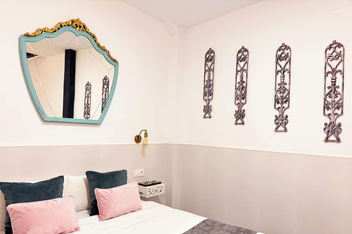 A bedroom with a bed, two pillows, a nightstand, a mirror, and decorative wall art.