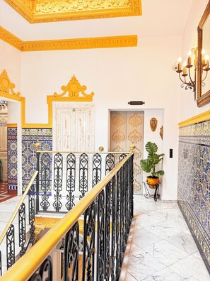 A grand staircase with ornate black railings and a golden handrail, leading to a door with intricate designs. - Palace House Hércules (Seville)