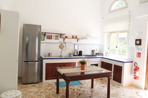 A kitchen with a refrigerator, stove, sink, wooden cabinets, and a window.