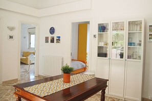 A room with a wooden table, a potted plant, a bed, and a wardrobe with glass doors.