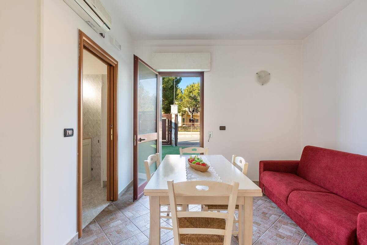 A dining area with a table, chairs, and a red sofa.
