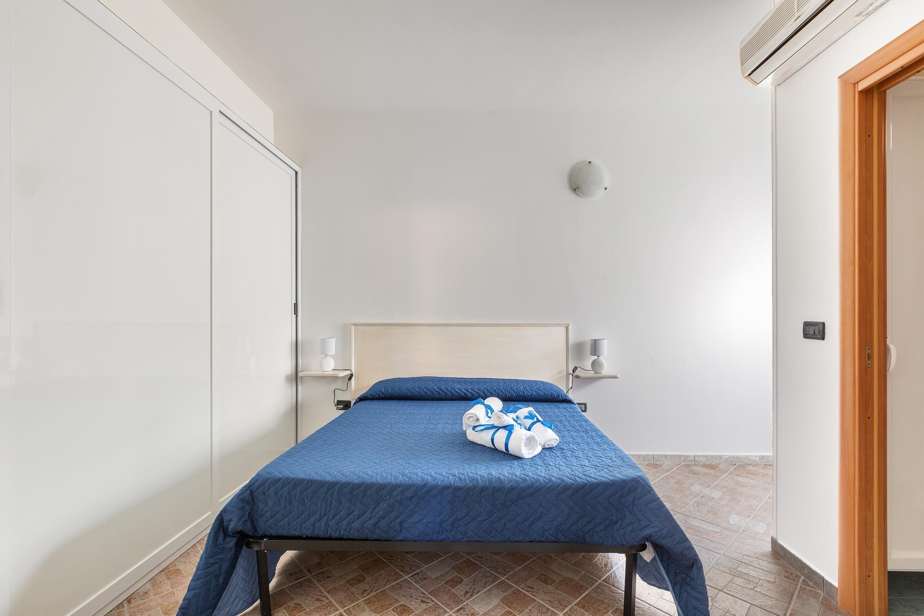 A hotel room with a bed, a wooden door, and a wall-mounted air conditioner.