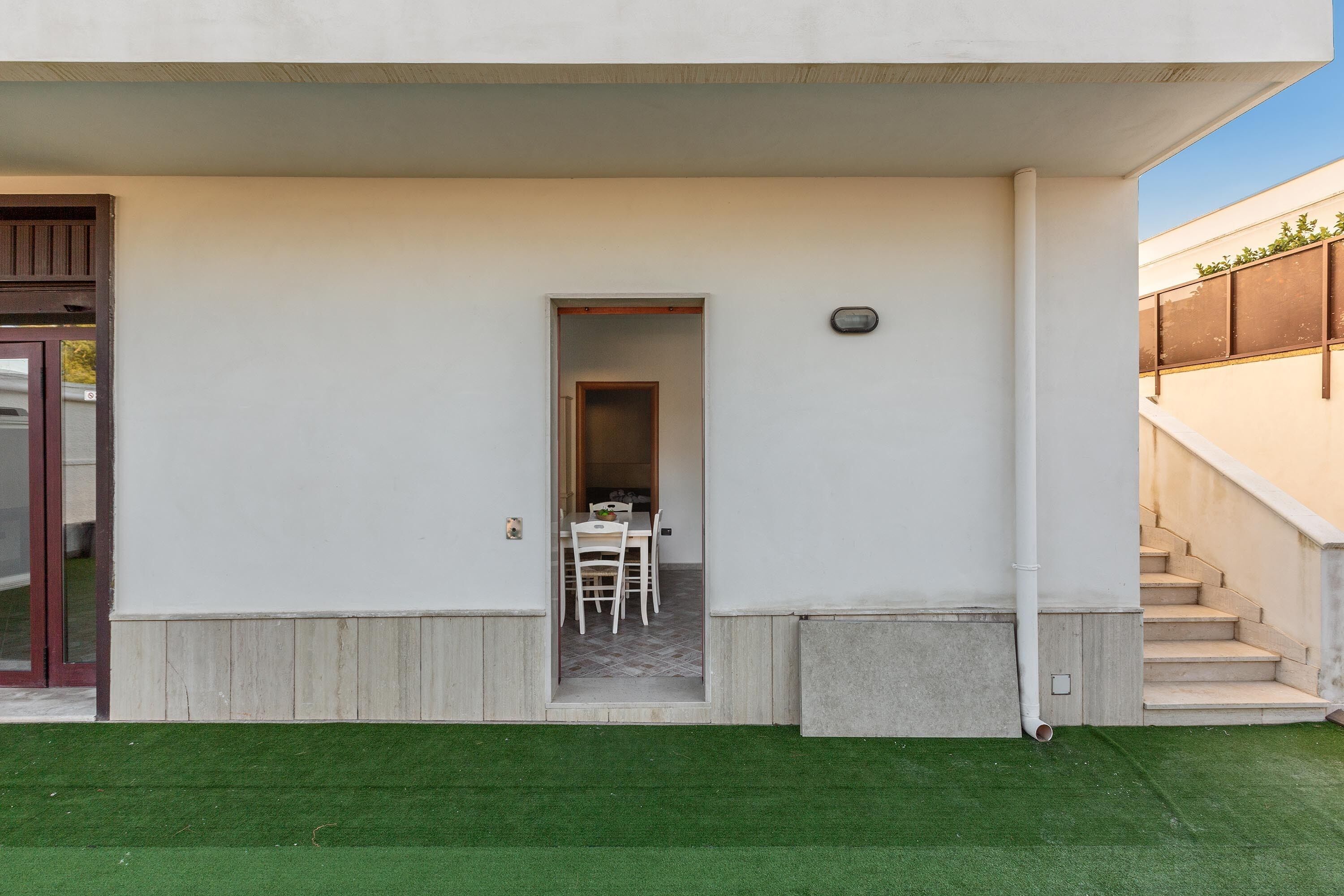 A modern building with a covered outdoor area, a staircase, and a door leading to an interior space.