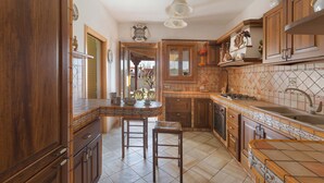 A kitchen with wooden cabinets, a tiled backsplash, and a central island with stools. - Villa Rosy (Maruggio)