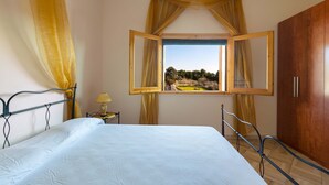 A bedroom with a bed, a window with curtains, a nightstand, and a wardrobe. - Villa Rosy (Maruggio)