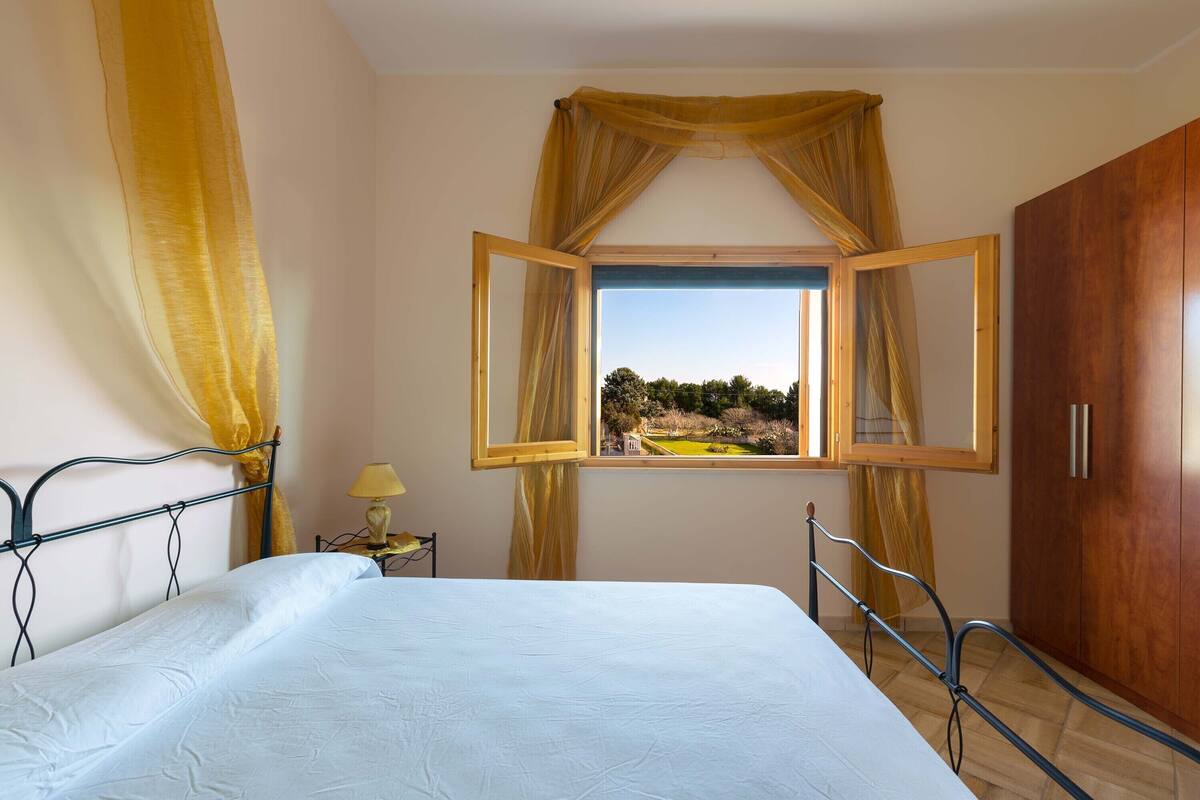 Un dormitorio con cama, cortinas en la ventana, una mesita de noche y un armario.