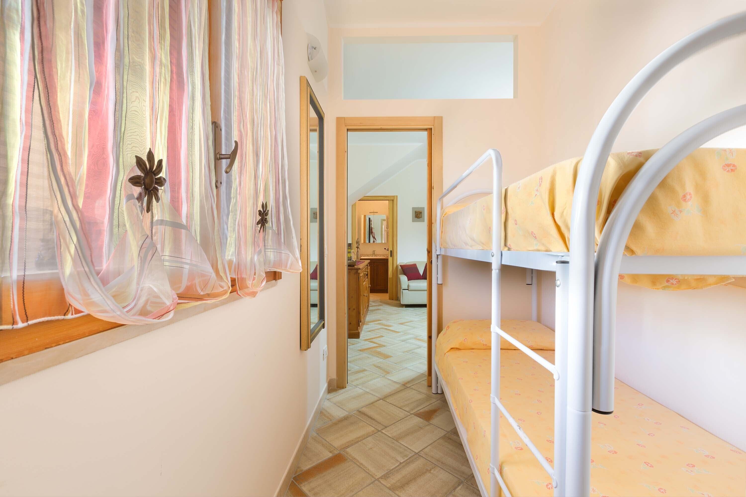 Un pasillo estrecho con literas a un lado y una puerta que da a otra habitación.
