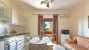 A modern kitchen with a dining table and chairs, a sofa, and an air conditioning unit. - Villa Rosy (Maruggio)