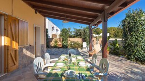 An outdoor patio with a table set for dining, surrounded by chairs, under a wooden pergola. - Villa Rosy (Maruggio)