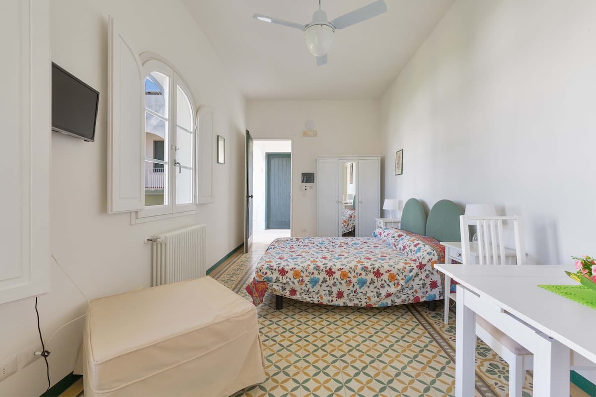 A bedroom with a bed, a desk, a chair, a ceiling fan, and a radiator.