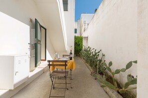 Un estrecho pasillo exterior con una mesa lista para dos personas, una silla y una botella de vino.