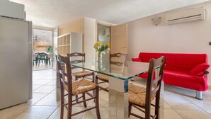 A dining area with a glass table and wooden chairs, a red sofa, and an air conditioning unit on the wall. - Residence Aquarium (Torricella)