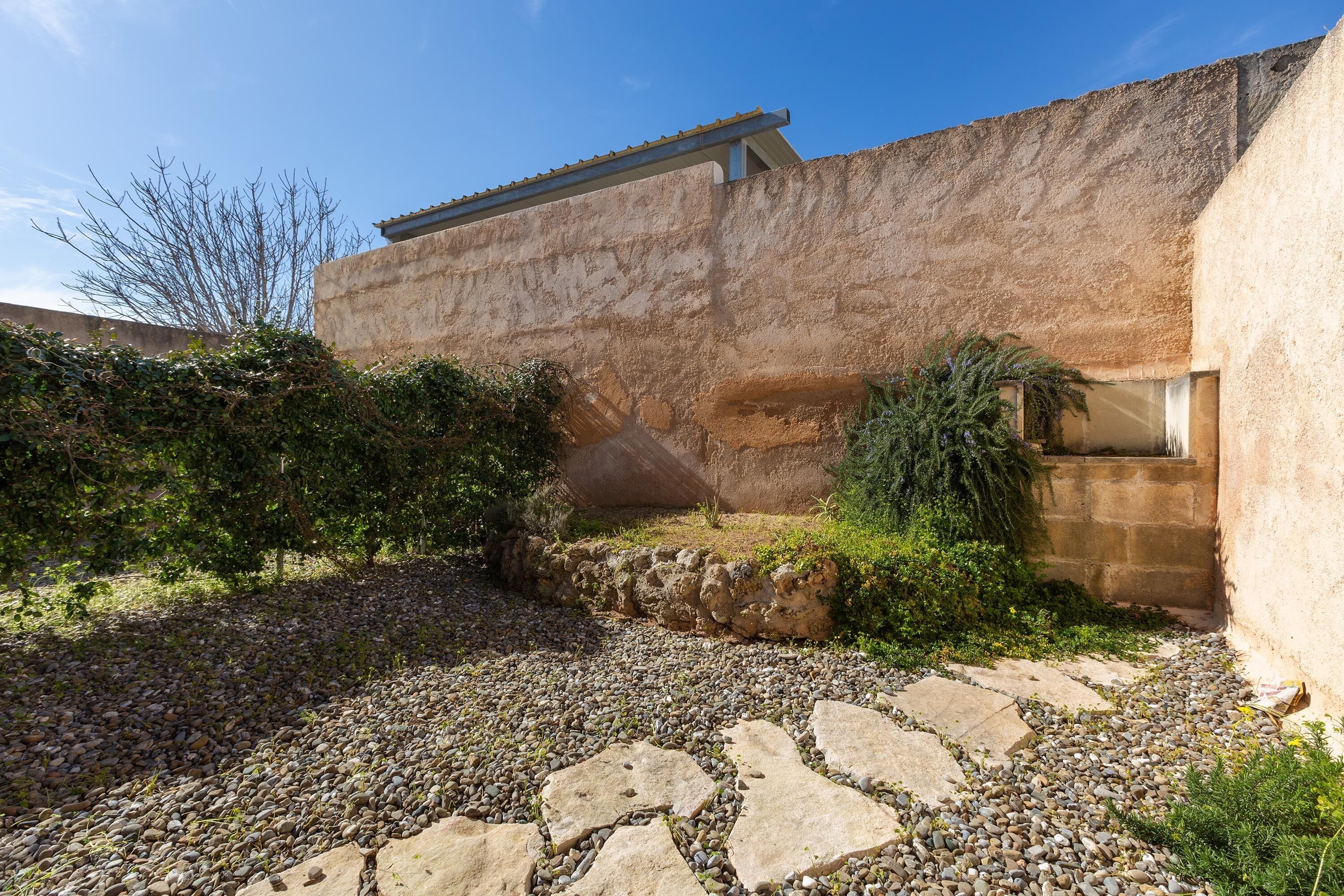 Un patio con un sendero de piedra, una pared rústica y una ventana.