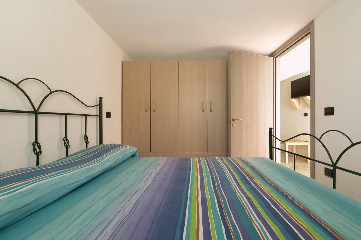 A bedroom with a bed, a wardrobe, and a door leading to another room.