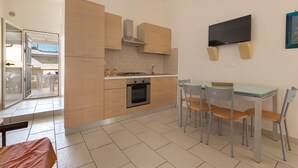 A modern kitchen with wooden cabinets, a built-in oven, a dining table with chairs, and a flat-screen TV mounted on the wall. - Residence Aquarium (Torricella)
