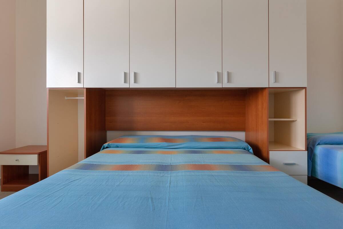A bedroom with a bed, a wooden headboard, a nightstand, and a wardrobe.