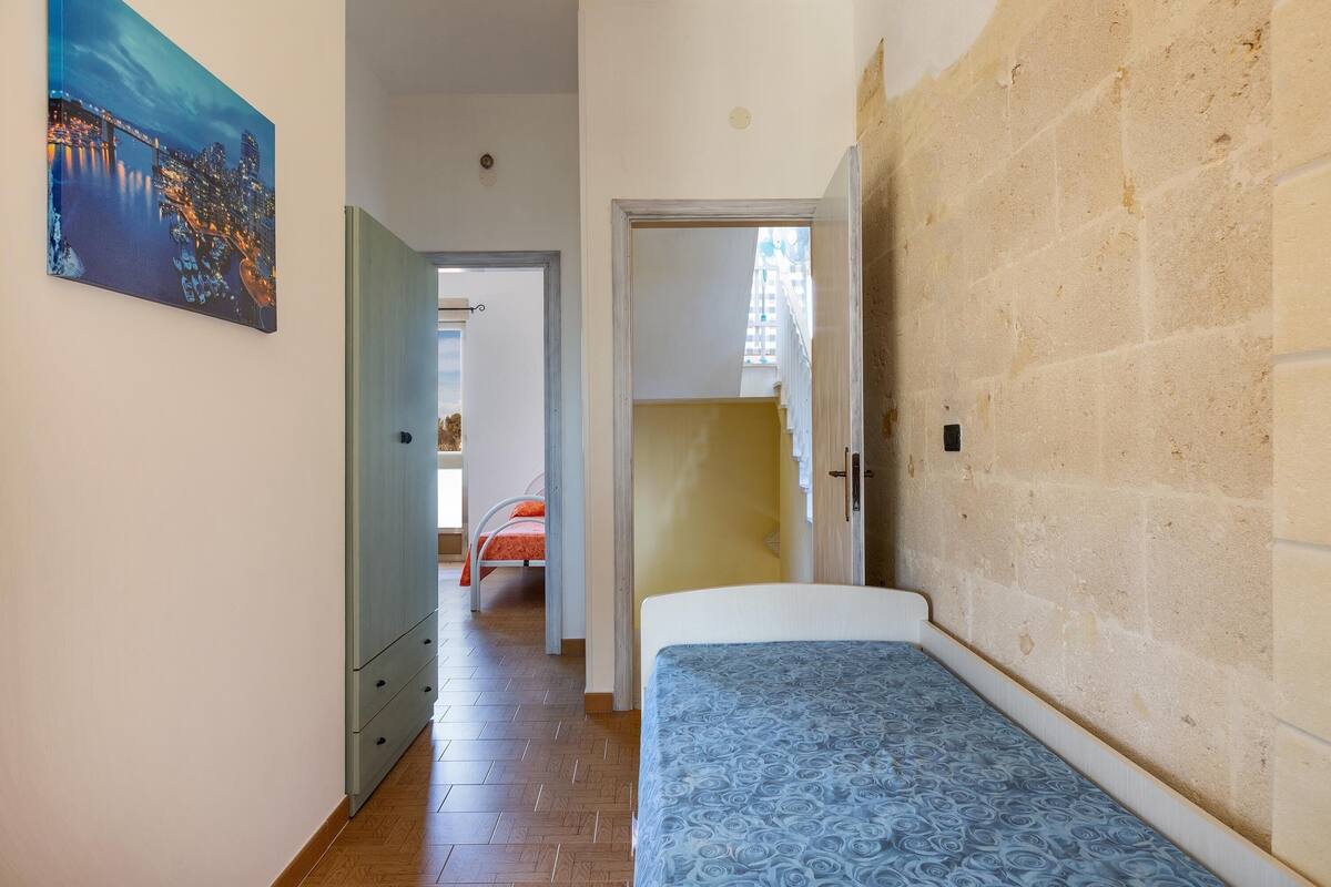 A bedroom with a bed, a painting, and a view of another room.