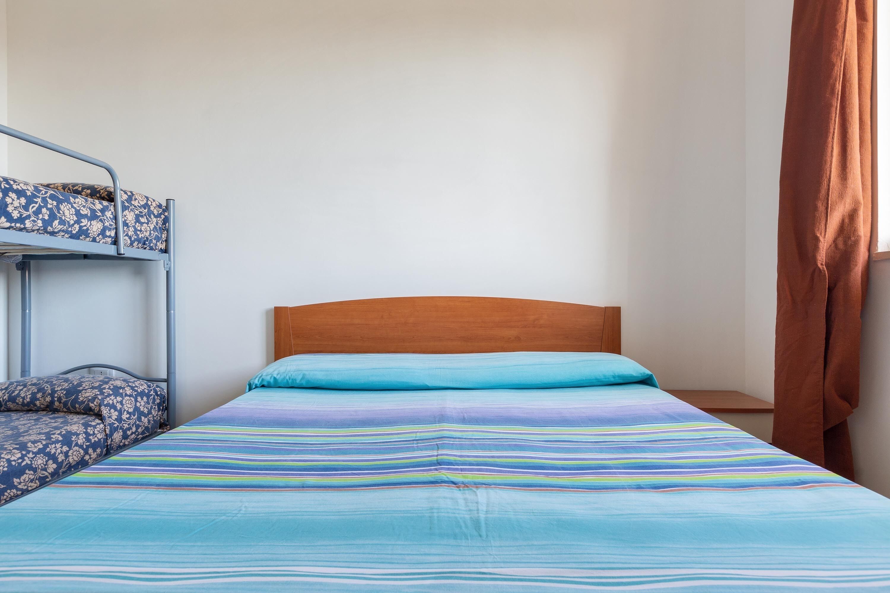A single bed with a wooden headboard, a bunk bed to the left, and a brown curtain on the right.